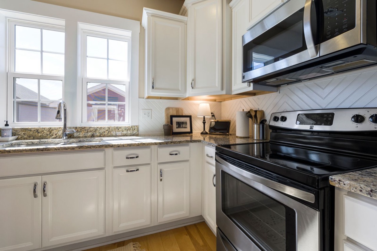 Corner of a kitchen with white cabinets, silver handles and a window above the sink